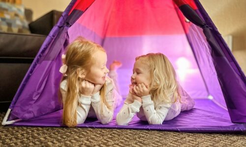 Two young girls relax inside a colorful tent available with the glamping add on package.
