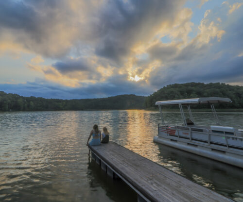 friends sitting on edge of deck at sunset