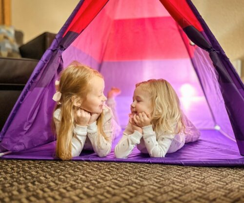 Two young girls relax inside a colorful tent available with the glamping add on package.